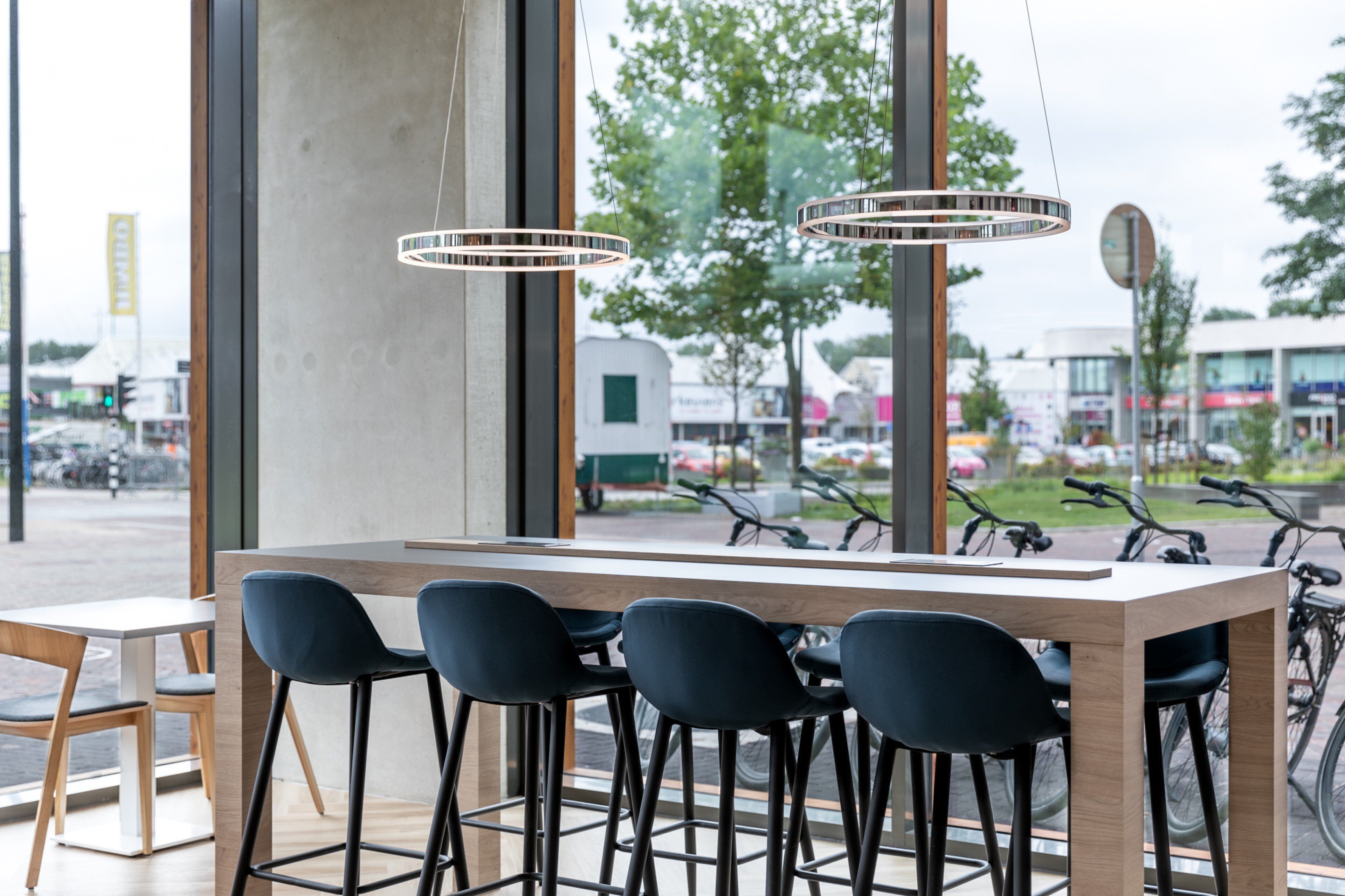 A modern bar area with a wooden table and black chairs, large windows with a view of bicycles and buildings outside.