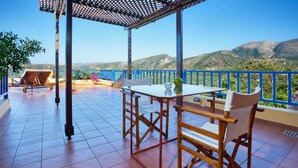 Eine Terrasse mit Tisch und Stühlen, einer Pergola und Blick auf Berge.