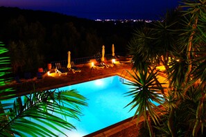 Ein Swimmingpool mit Liegestühlen und Sonnenschirmen, umgeben von Palmen.