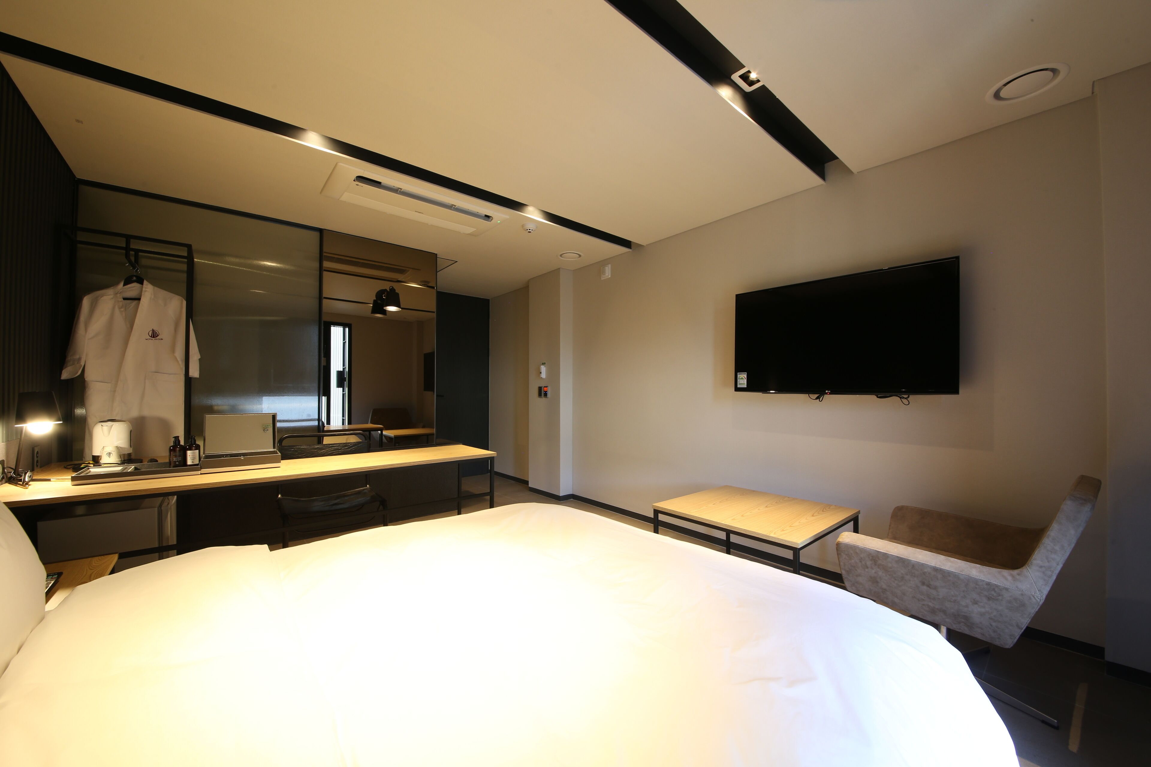 Una habitación de hotel moderna con una cama grande, un escritorio con una computadora portátil, una silla, un televisor montado en la pared y un espejo.