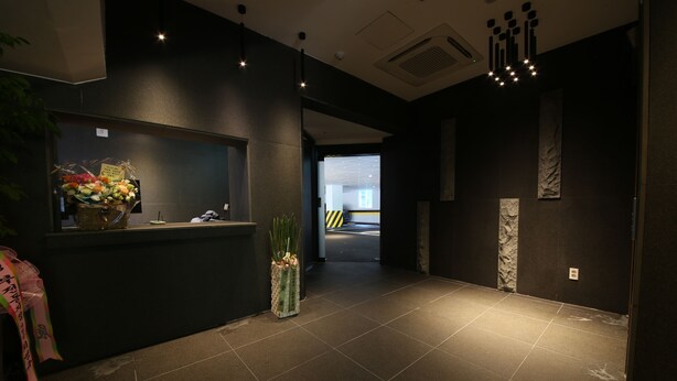 A reception area with a dark-toned reception desk, a potted plant, and a corridor leading to another section. - Hotel Yeoubi (Busan)