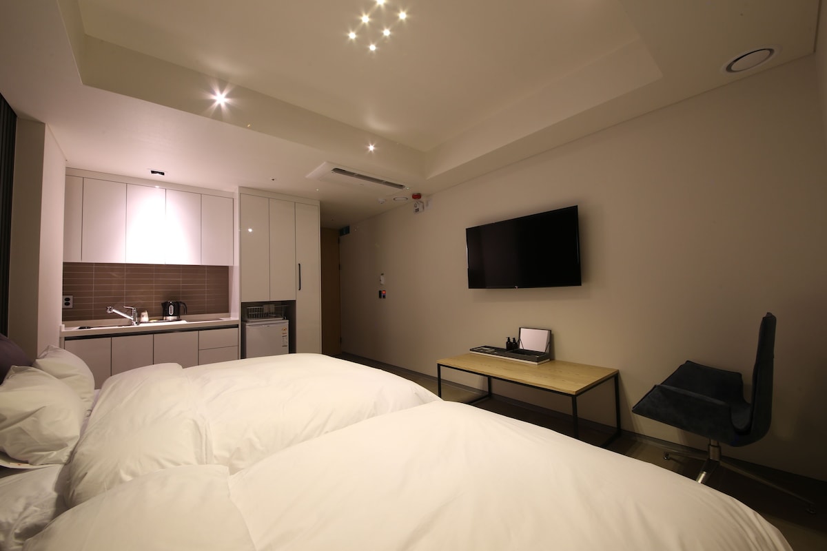 A hotel room with a bed, a desk, a TV, and a kitchenette.
