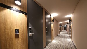 A hotel hallway with a carpeted floor, wooden and dark-colored walls, and a series of doors with a number sign above one. - Hotel Yeoubi (Busan)