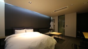 A modern hotel room with a large bed, a bedside table, a chair, and a small table. - Hotel Yeoubi (Busan)
