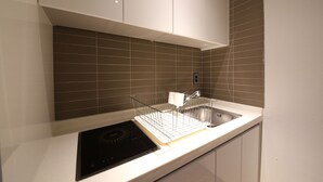 A modern kitchen with a black induction cooktop, a stainless steel sink, and a white countertop. - Hotel Yeoubi (Busan)