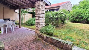 Ein überdachter Patio-Bereich mit einer Steinpfeiler, einem Pflasterweg und einer Rasenfläche.