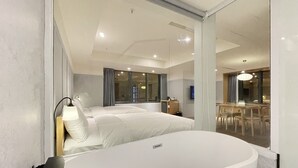A modern hotel room with a large white bathtub, a bed with white linens, a desk, and a dining area with chairs and a table. - Green Hotel - midori (Taichung)