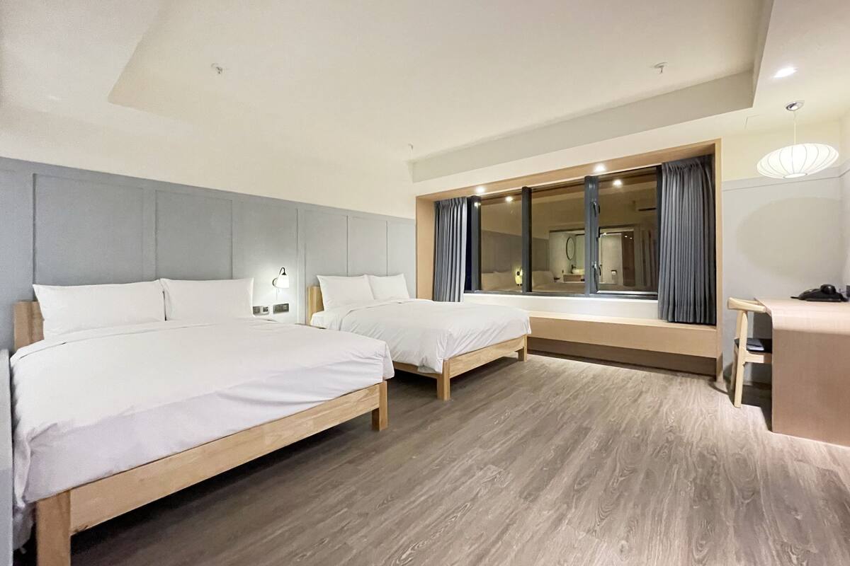 A modern hotel room with two single beds, a large mirror, and a desk with a chair.