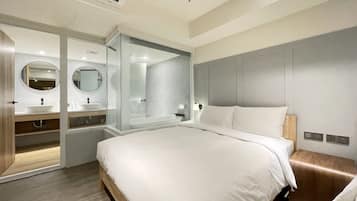 Una habitación de hotel moderna con una cama grande, un tocador con espejo y una zona de ducha.