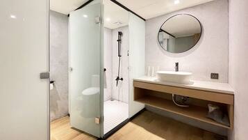 A modern bathroom with a glass-enclosed shower, a round mirror, and a wooden vanity.