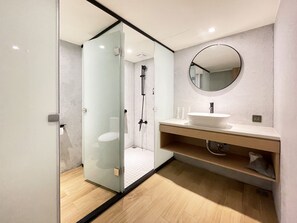 A modern bathroom with a glass-enclosed shower, a round mirror, and a wooden vanity. - Green Hotel - midori (Taichung)