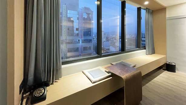 A modern room with a large window, a desk with a lamp, and a view of the cityscape. - Green Hotel - midori (Taichung)