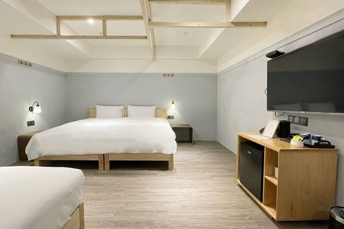 A modern hotel room with a wooden bed, a TV, and a small desk with a lamp.