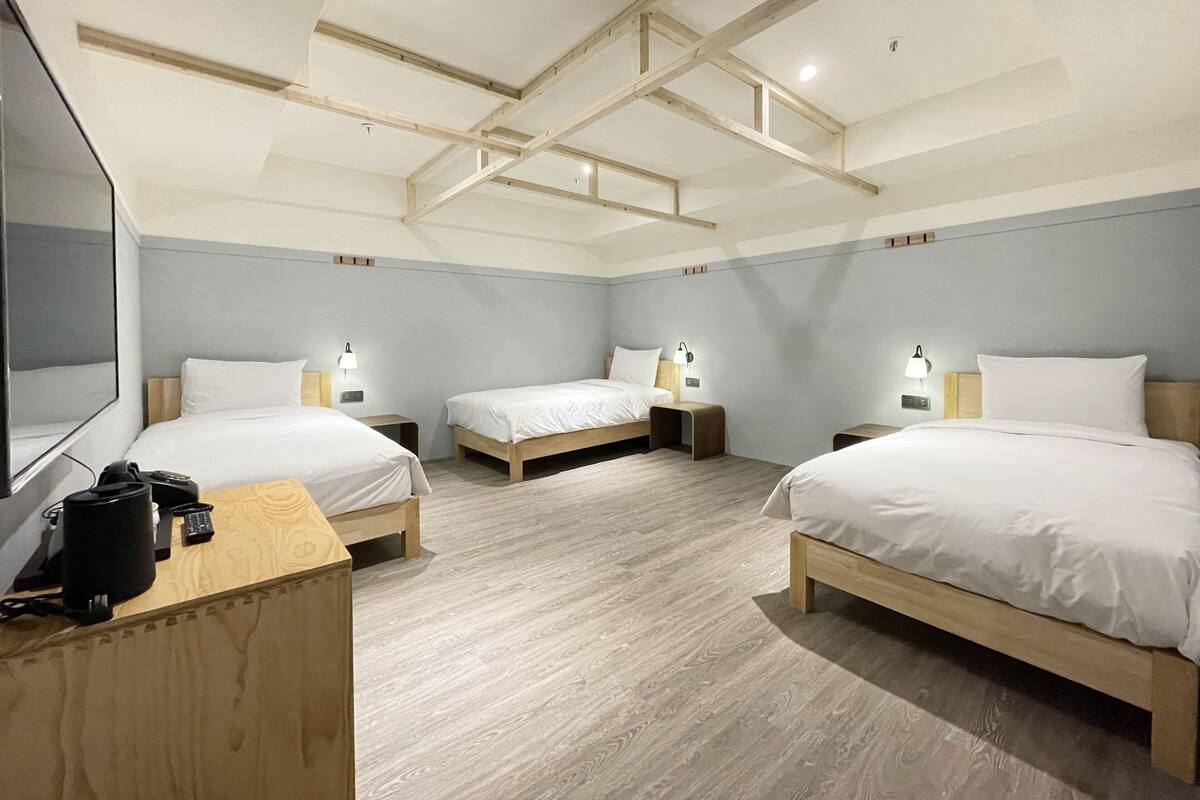 A hotel room with three beds, wooden headboards, and bedside tables with lamps.