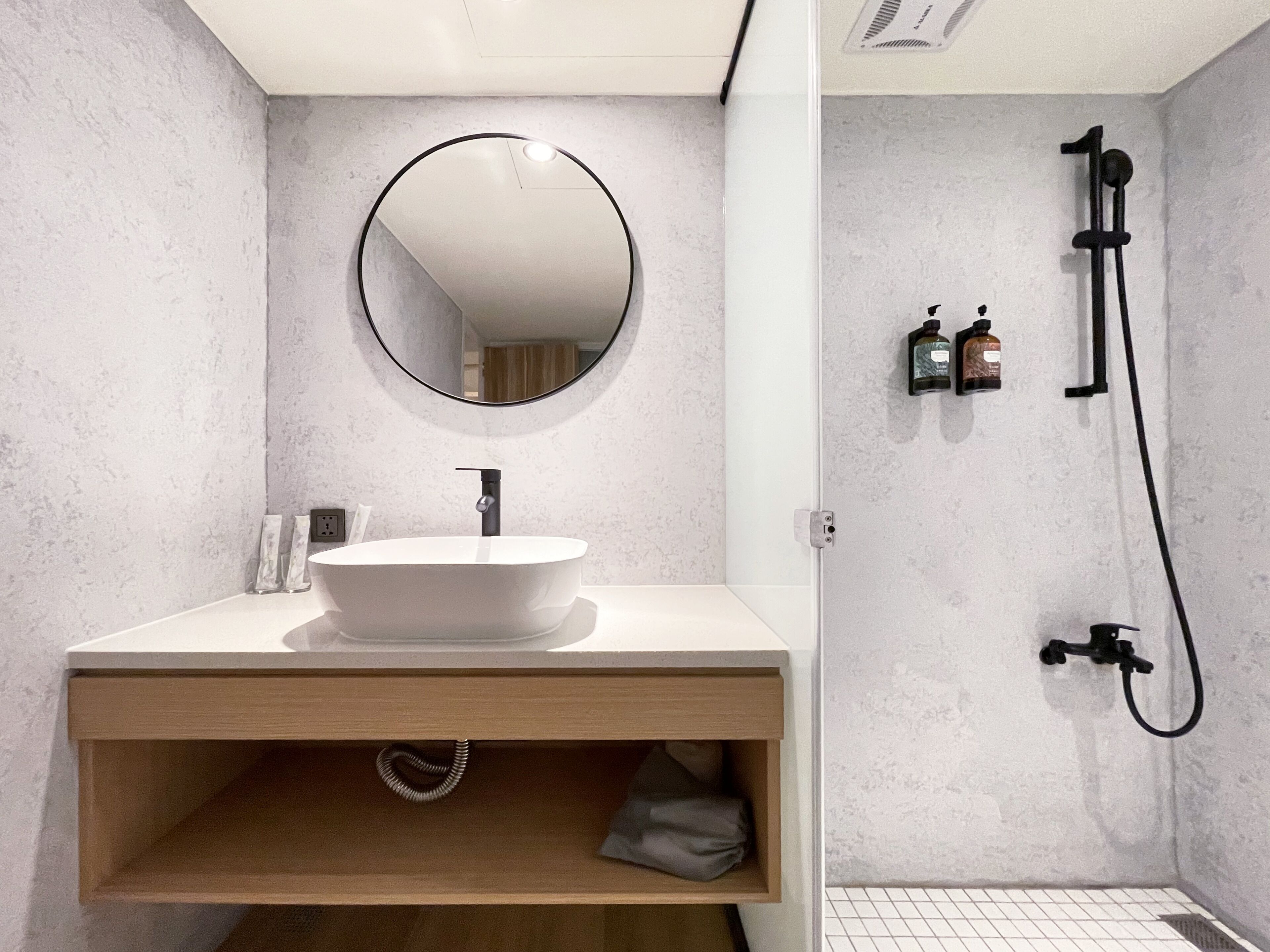 A modern bathroom with a round mirror, a white sink, and a shower area.