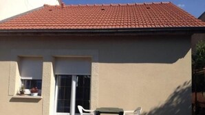 Un bâtiment doté d’un toit recouvert de tuiles rouges, d’une façade de couleur beige et d’un petit patio avec une table et des chaises.