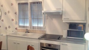 Une cuisine de taille réduite avec des meubles blancs, un évier, un four à micro-ondes et une cuisinière.
