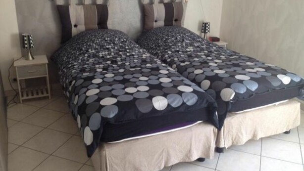 Un lit double avec une couette à pois noirs et blancs, une table de chevet avec une lampe et une tringle à rideaux fixée au mur.