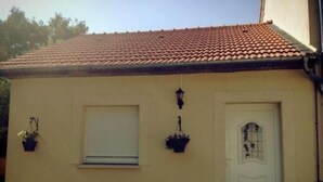 Un petit bâtiment avec un toit recouvert de tuiles, une porte blanche et deux fenêtres.