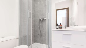 Ein modernes Badezimmer mit einer begehbaren Glasdusche, einer weißen Toilette und einem Waschtisch mit Pflegeprodukten.