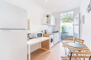 A modern kitchen with white cabinetry, a microwave, a kettle, and a washing machine. There is a dining area with a wooden table and chairs. - MaisonMars Studio 4 Blancarde (Marseille)