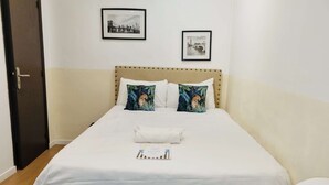 Ein ordentlich bezogenes Bett mit weißer Bettwäsche und zwei Kissen mit Leopardenmuster, ein gerahmtes Stadtbild an der Wand und ein gerahmtes Bild einer Brücke.