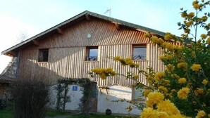 Une maison en bois avec un toit en pente, un petit balcon et un jardin où poussent des fleurs jaunes.
