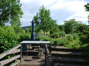 An outdoor seating area with a table and chairs, surrounded by greenery and a wooden fence.