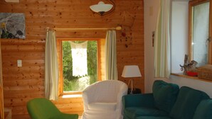 Une pièce chaleureuse avec des murs en bois, un fauteuil vert, un fauteuil blanc et un canapé de couleur turquoise.