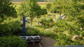 Un jardin avec une table et des chaises, un toboggan et une vue sur un paysage vallonné.