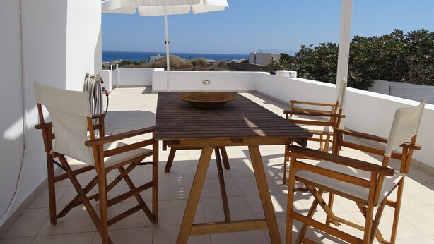 Una mesa de madera con sillas y un paraguas blanco en una terraza con vistas al mar.