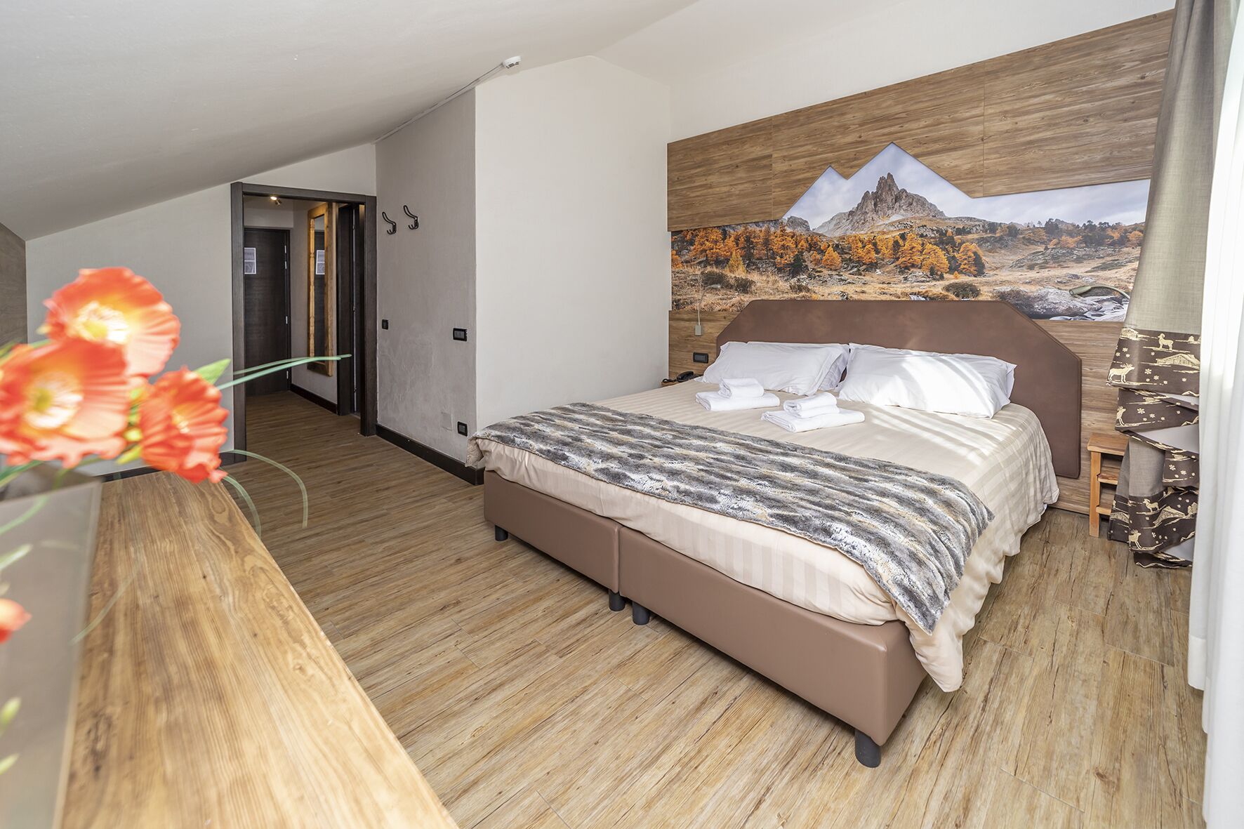 Een moderne hotelkamer met een groot bed, een houten vloer, een schilderij van een berglandschap en een houten hoofdbord.