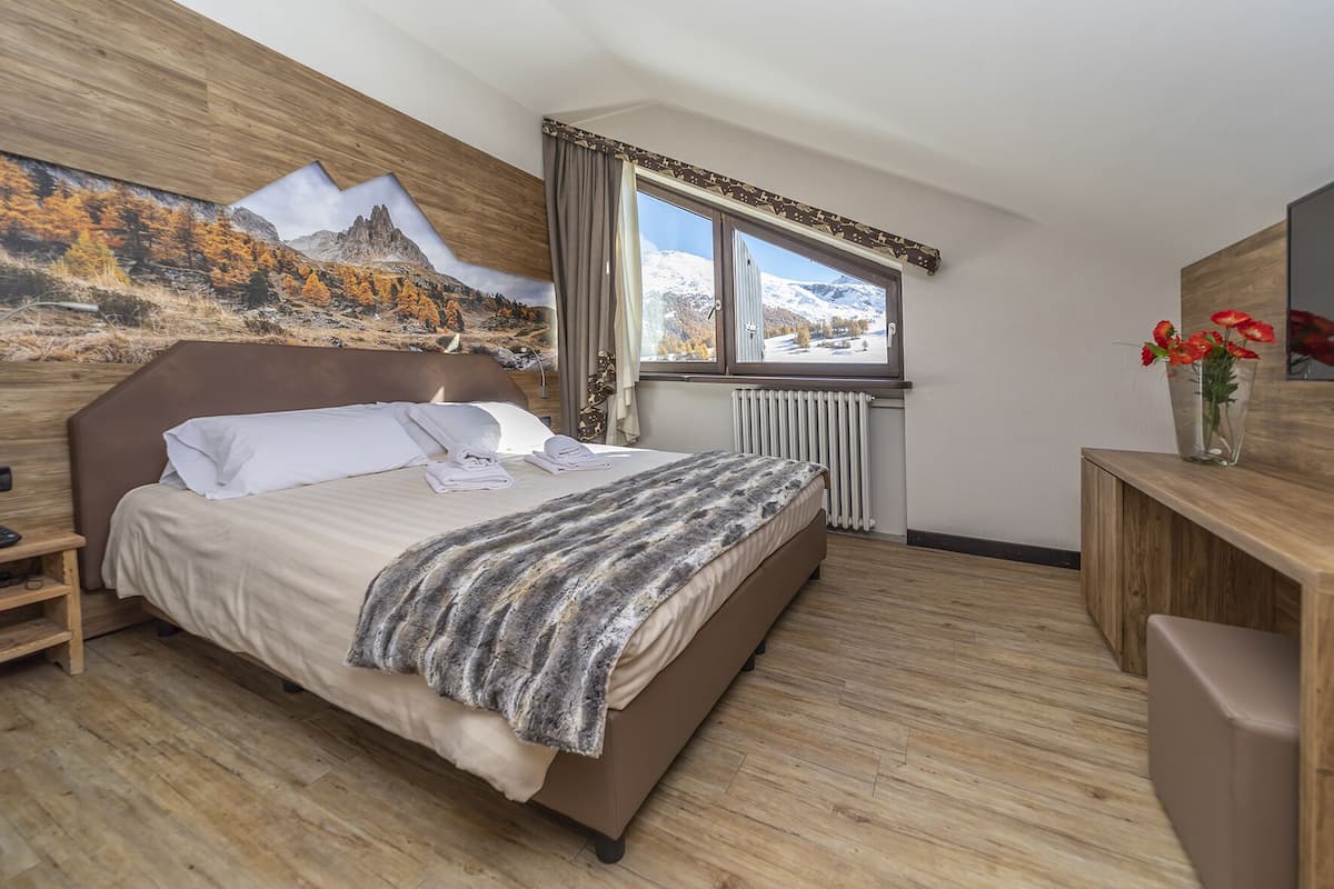 Un dormitorio moderno con una cama grande, cabecera de madera, ventana con vistas a la montaña, radiador y escritorio con un florero.