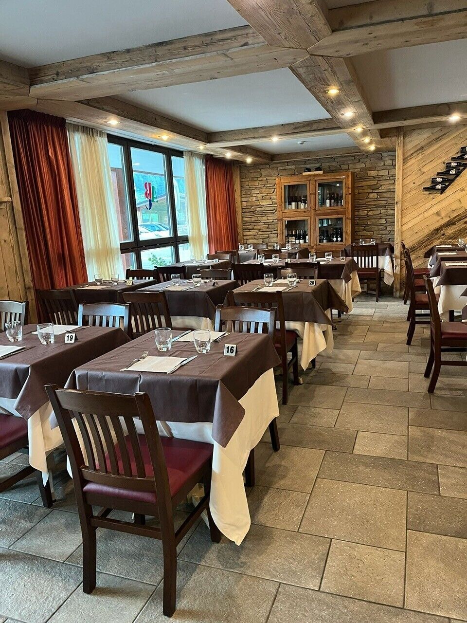 A restaurant with stone walls, wooden beams, and tables set for dining.