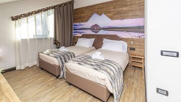 Habitación doble con dos camas, suelo de madera, un cuadro en la pared y cabecero de madera.