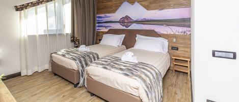 A double room with two beds, wooden flooring, a painting on the wall, and a wooden headboard.