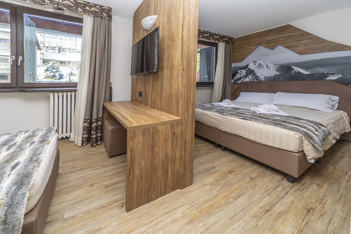 Un dormitorio con cama, escritorio, televisión y un mural de montañas en la pared.