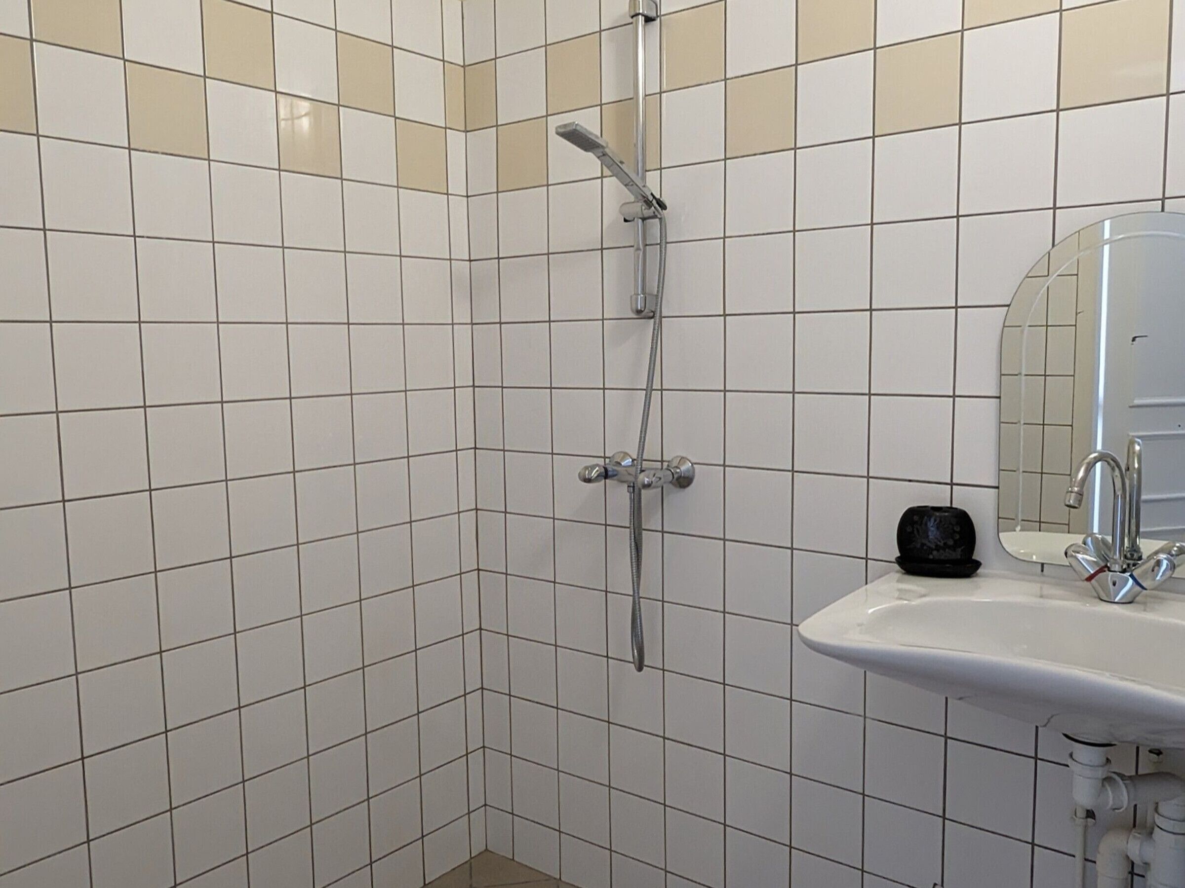 Een badkamer met witte betegelde wanden, een douche met handdouche en een wastafel met spiegel erboven.