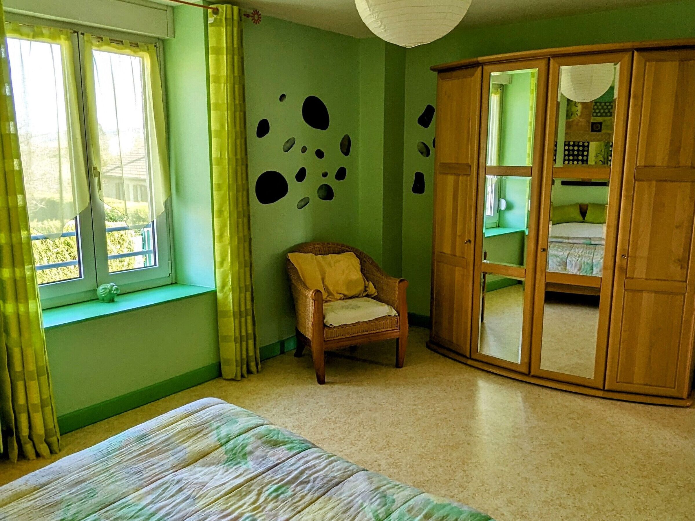 Ein Zimmer mit einem Bett, einem Sessel, einem Schrank und einem Fenster mit Vorhängen.