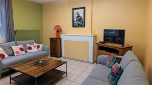 A living room with a grey sofa, a wooden coffee table, a TV on a wooden stand, and a fireplace. - Cozy gîte in Mécrin - 10 guests (Mécrin)