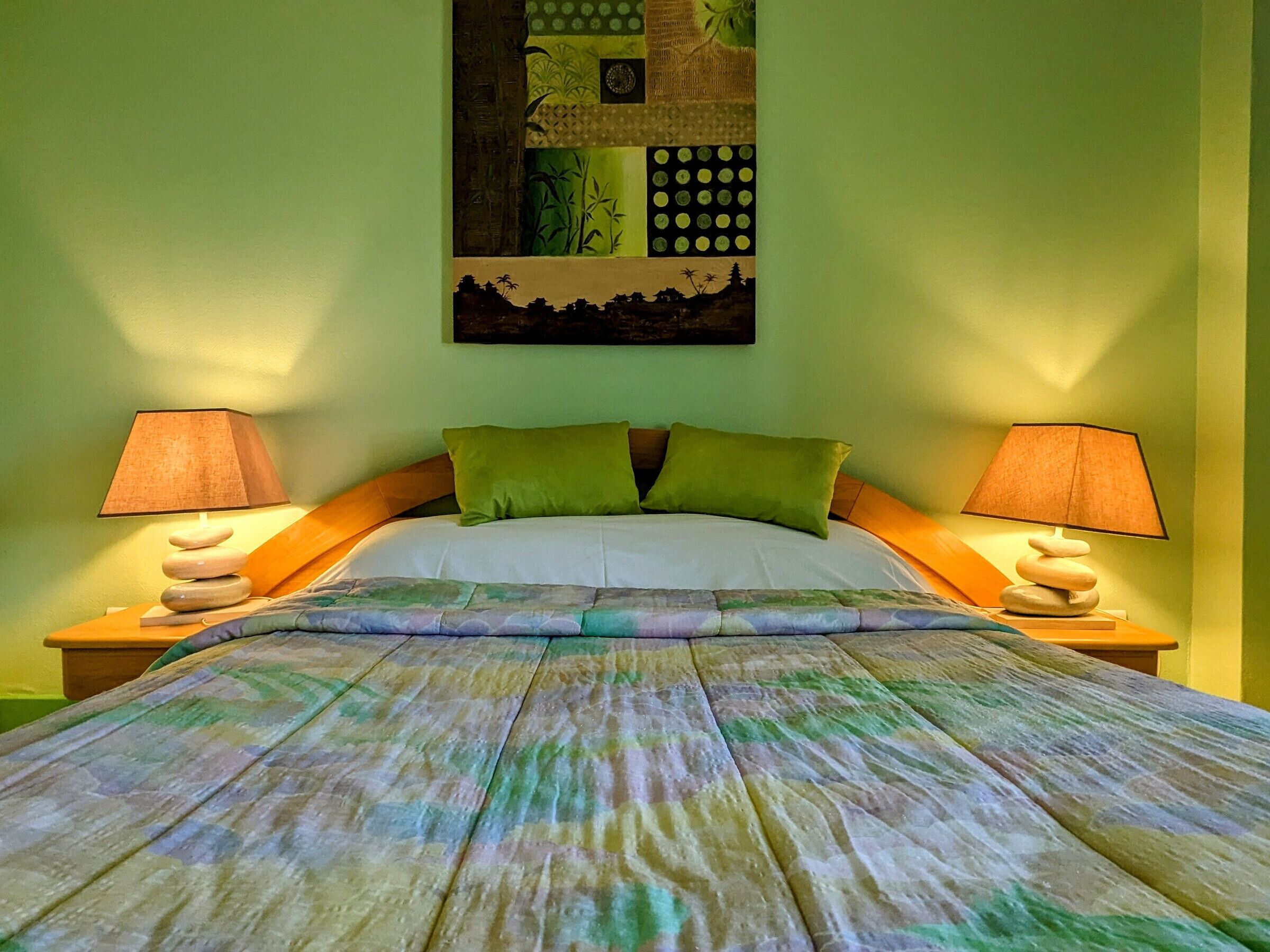 A neatly made bed with green pillows, two bedside lamps, and a wall art piece above the bed.