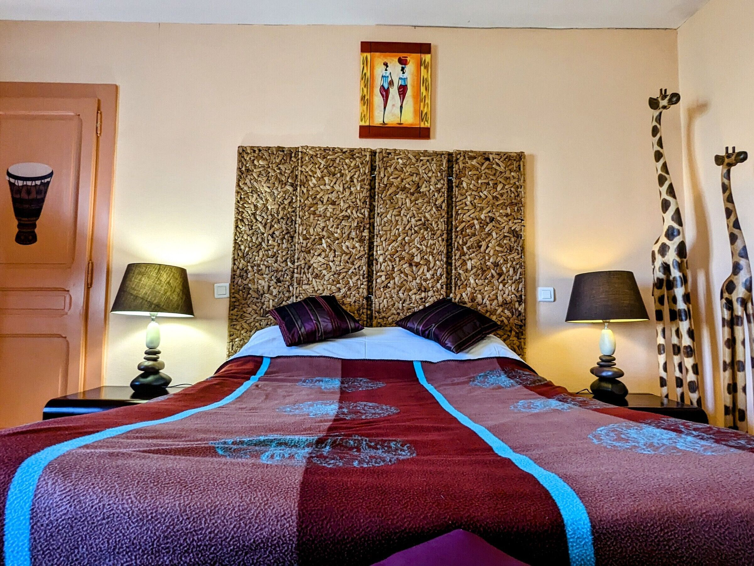 A hotel room with a large bed, two nightstands, a headboard with a wood pattern, a painting above the bed, and a giraffe statue on the right.