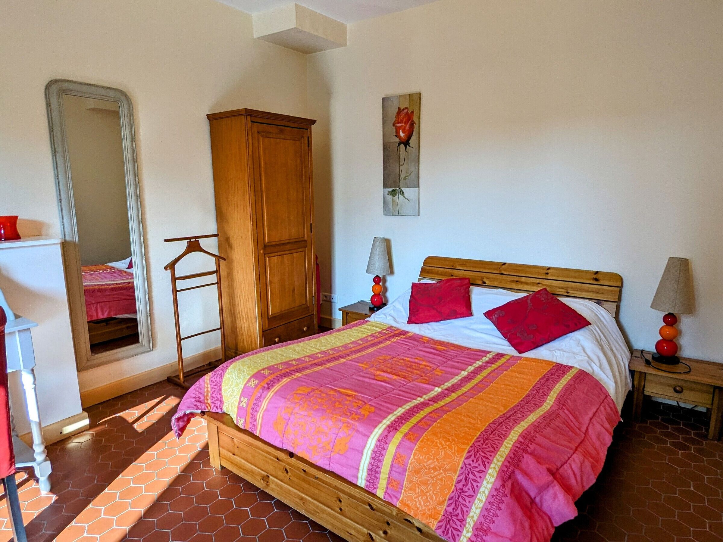 A bedroom with a wooden bed, a wardrobe, a mirror, and a painting on the wall.