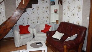 A room with a sloped ceiling, two white armchairs with red cushions, a red leather sofa with white cushions, and a small white table with a remote control.