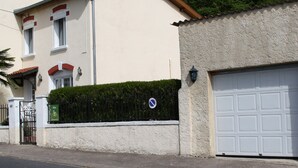 A two-story residential building with a garage, a gated entrance, and a hedge.