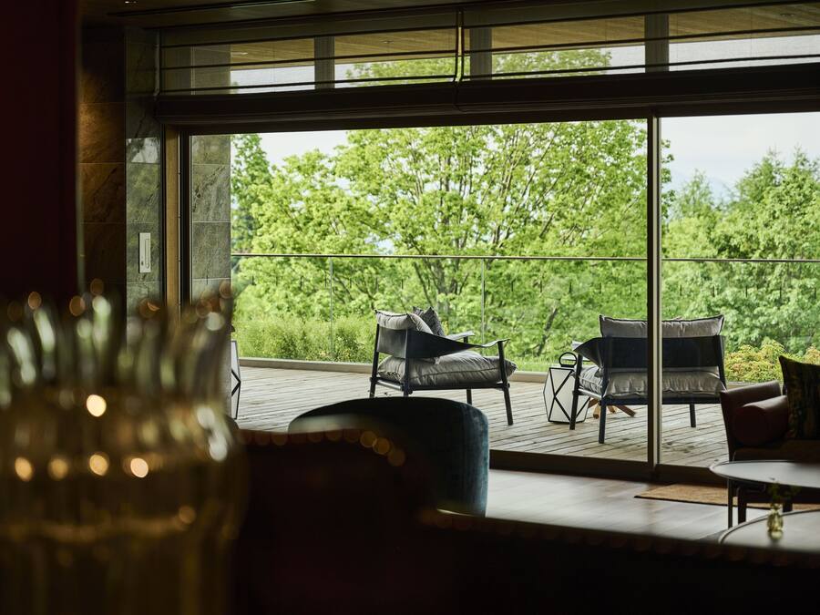 A room with a large window overlooking a deck with two chairs and a table.