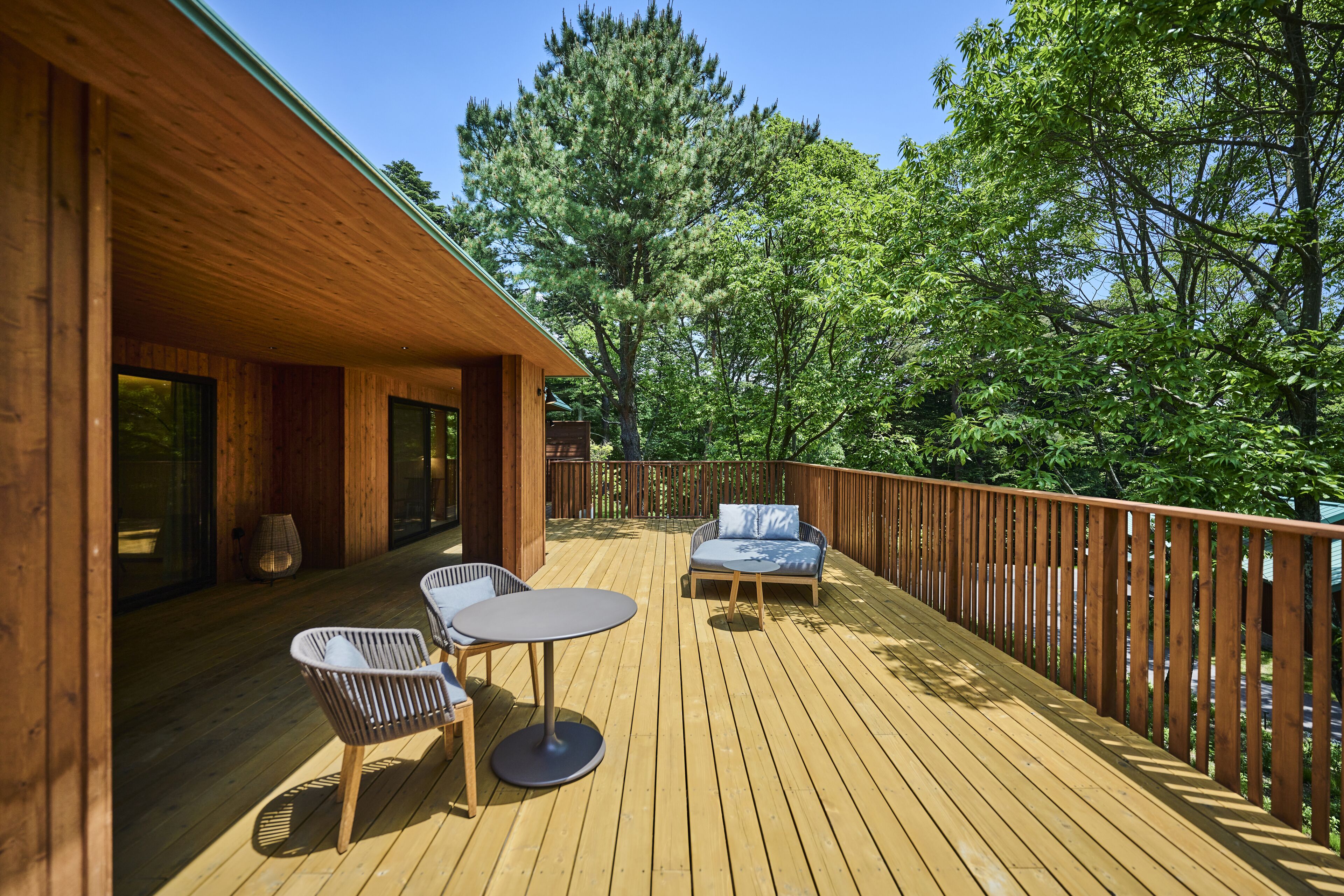Una terraza de madera con una mesa y sillas, rodeada por una barandilla de madera y árboles.