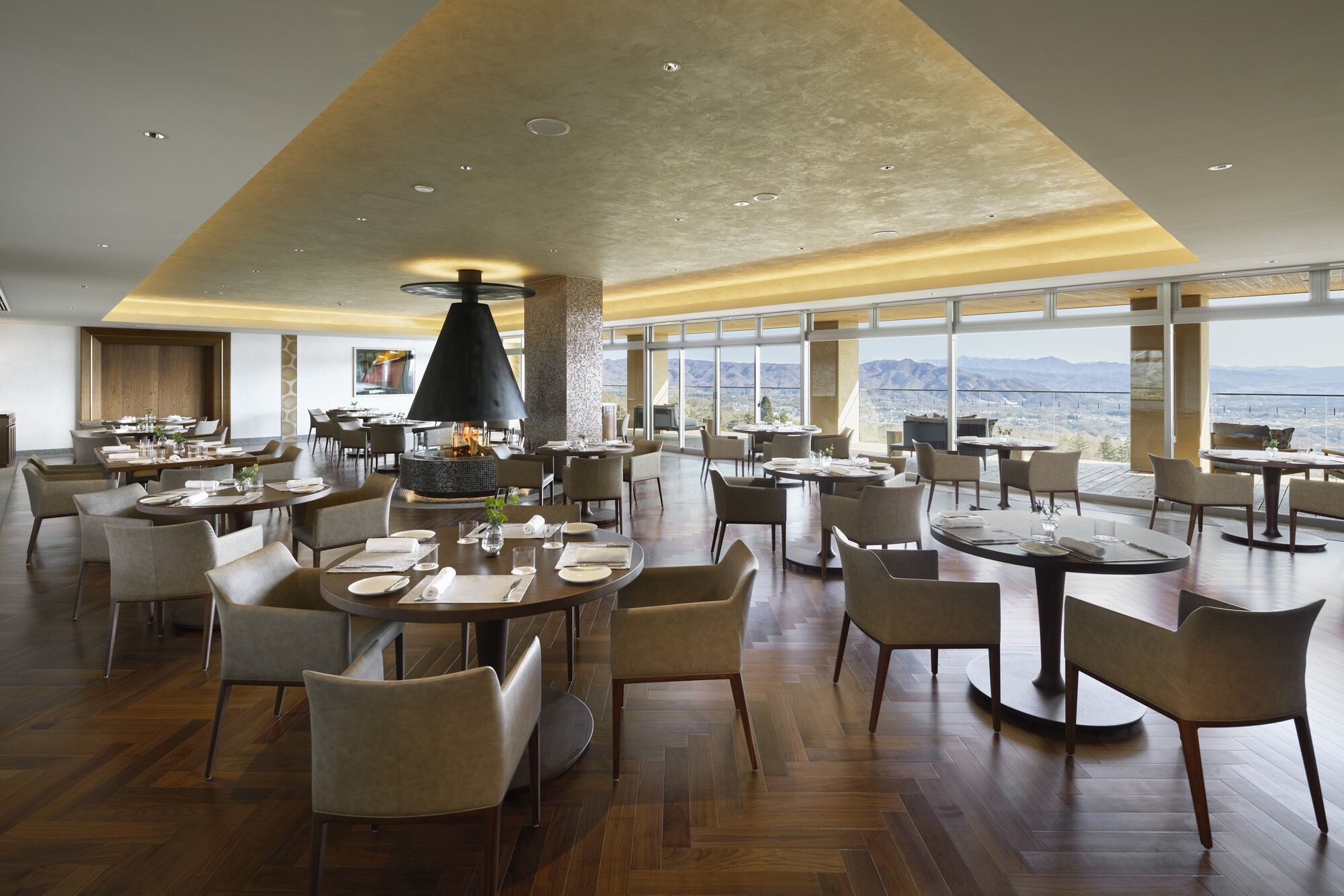 Ein geräumiges Restaurant mit mehreren Essbereichen, einem zentralen Kamin und großen Fenstern mit Blick auf die Berge.