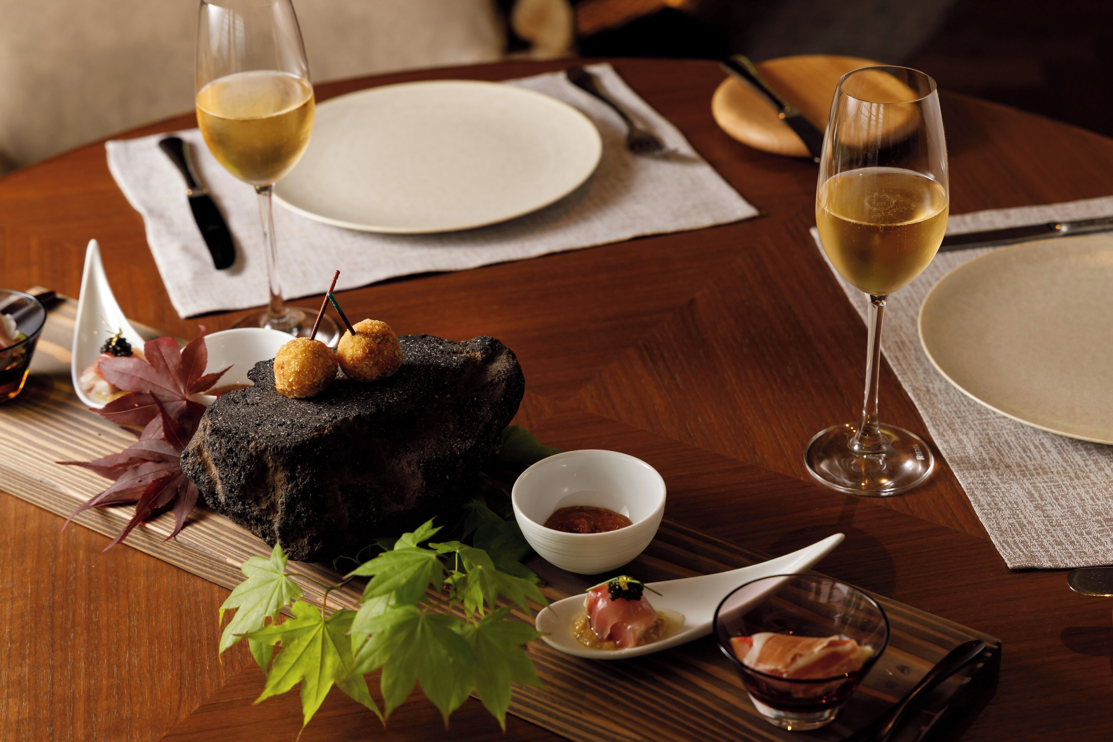 Une table de salle à manger en bois, avec une assiette de nourriture, deux verres de vin blanc et un bol de sauce.