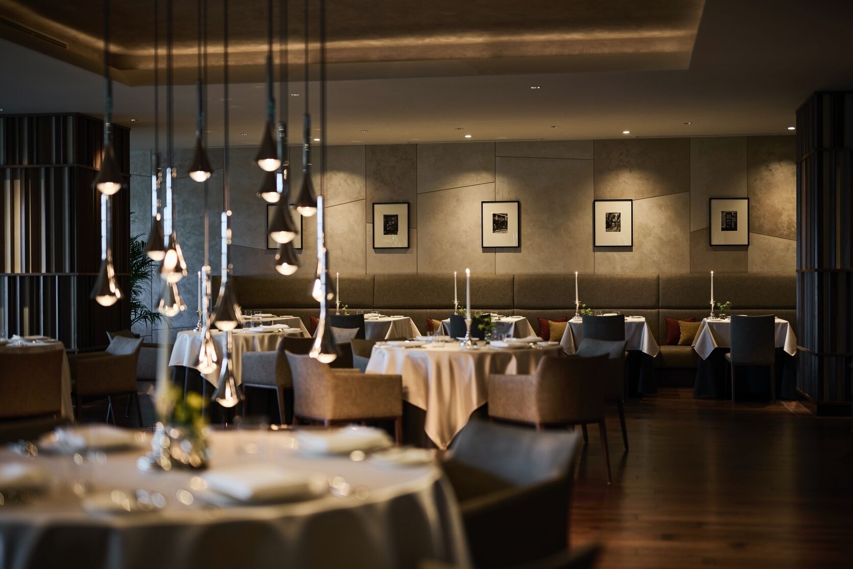 Ein Restaurant mit gedeckten Tischen, hängenden Pendelleuchten und gerahmten Bildern an der Wand.